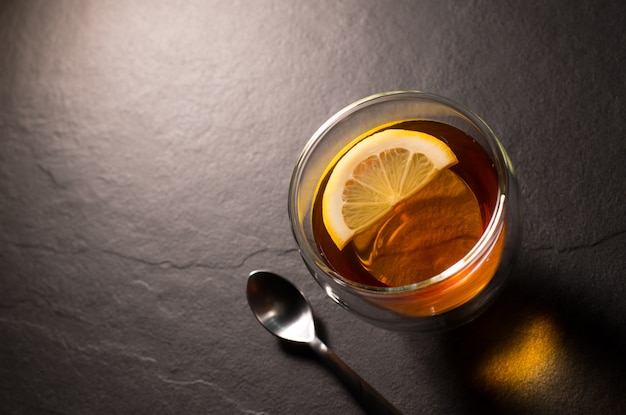 Top view image of a cup of tea with lemon on black granite background