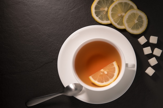 Top view image of a cup of tea with lemon on black granite wall