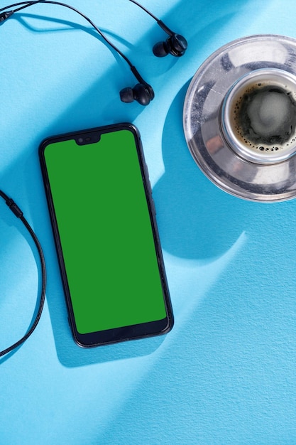 Top view image of smartphone with blank screen headphones and coffee cup