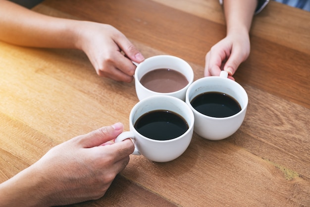 Top view image of three people clinking coffee cups on wooden table in cafe