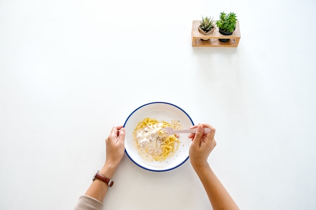 Top view image of a woman eating carbonara spaghetti on the table