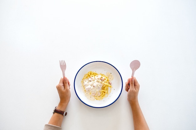 Top view image of a woman holding spoon and fork, preparing to eat carbonara spaghetti on the table