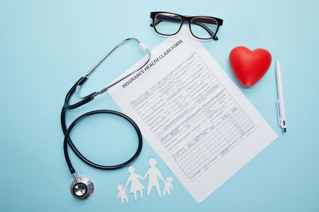 Top view of insurance health claim form, eyeglasses, paper cut family, red heart symbol and