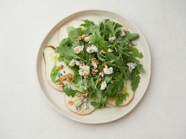 Top view isolated plate of salad with arugula, pear, blue cheese and walnuts