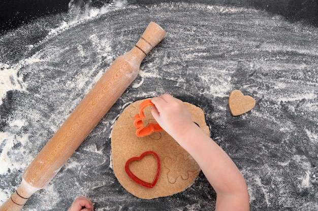 Top view of kid's hands with dough, rolling pin and dough