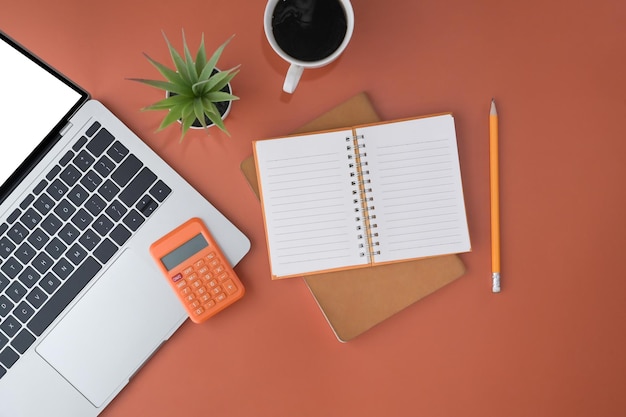 Top view laptop blank notebook coffee cup and calculator on orange background