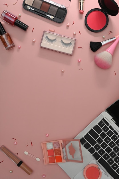 Top view laptop makeup brushes and cosmetics on pink background Feminine workspace