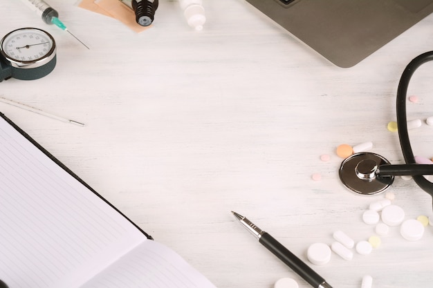 Top view of laptop, notepad, stethoscope, medicine bottles and syringe