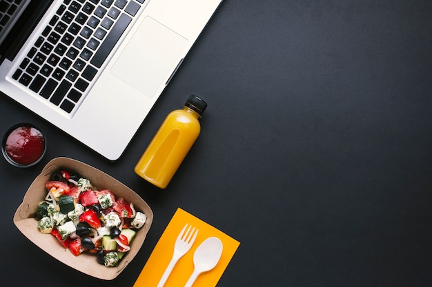 Top view laptop and salad on black background