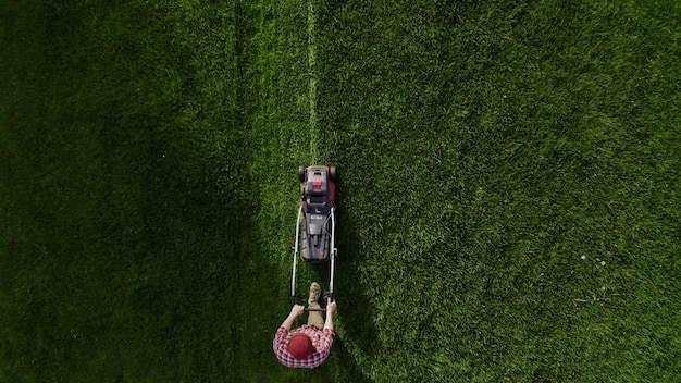 Top view of the lawnmover worker cutting green grass garden unknown man worker cutting grass with la