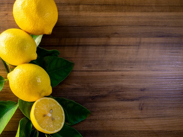 Top view of lemon and green leaves on wooden background