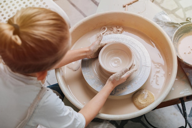 Top view of a little boy shaping clay vase on a pottery wheel in a workshop