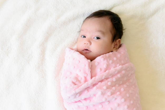 Top view of a little cute Asian baby girl wrapped up Wrapped in pink cloth lying on bed