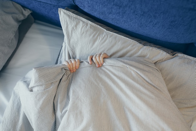 Top view of little kid in bed covering his face with blanket. Morning