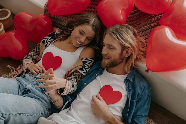 Top view of loving couple holding valentines cards while leaning on bed surrounded with red balloons