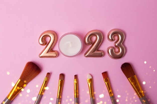 Top view of the makeup brushes on pink backgroundRose gold numbers 2023 above