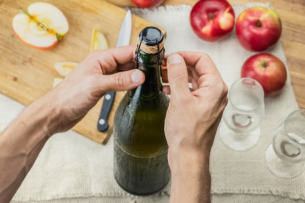 Top view of male hands opening bottle of premium cidre. Shot from above of uncorking beautiful ice cold bottle of apple wine