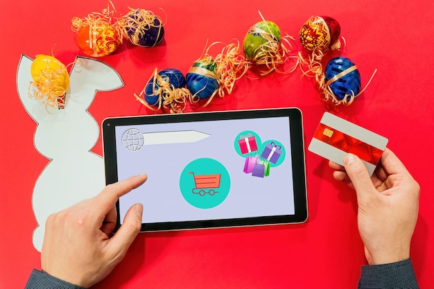 Top view of male hands with tablet credit card and easter eggs paper rabbit