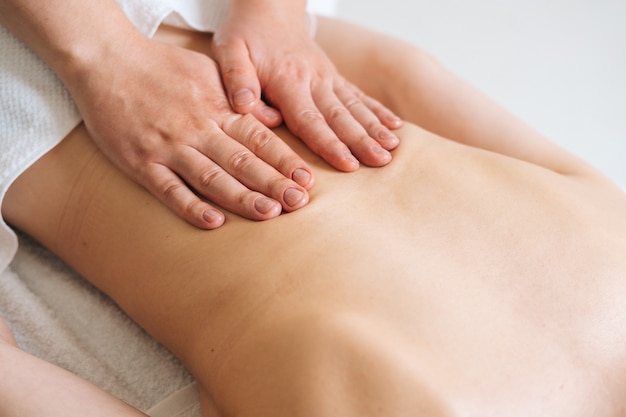 Top view of male masseur massaging back of young unrecognizable woman lying on massage table