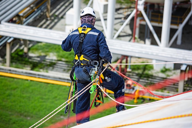 Top view male worker inspection wearing safety first harness rope safety line working at a high place on tank roof spherical gas