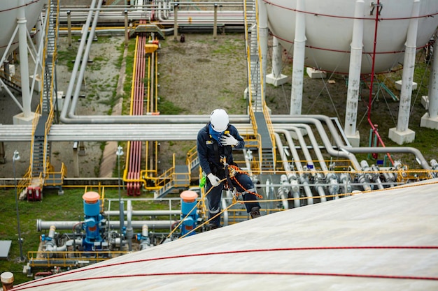 Top view male worker inspection wearing safety first harness rope safety line working at a high place on tank roof spherical gas