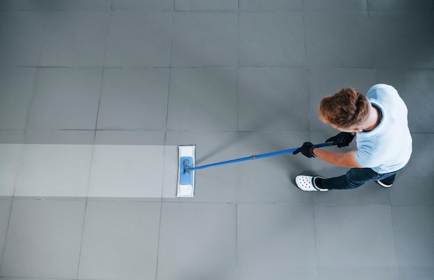 Top view of man in blue shirt and protective gloves that uses vacuum cleaner