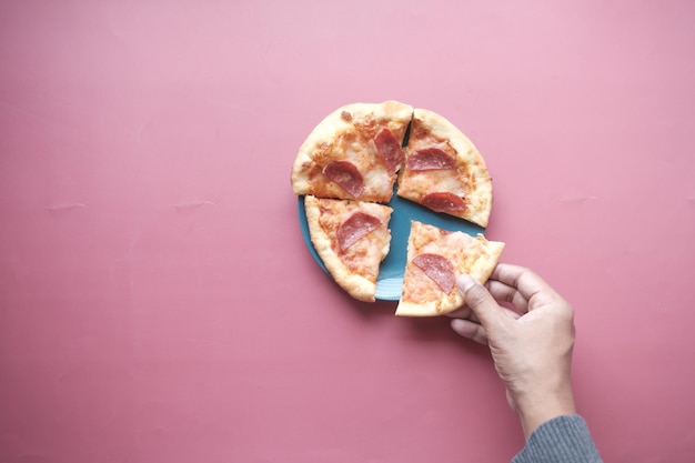 Top view of man hand picking slice of pizza from a plate