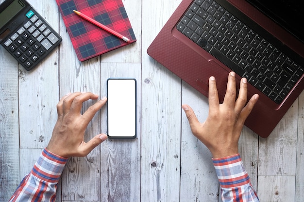 Top view of man hand using smart phone and typing on laptop .