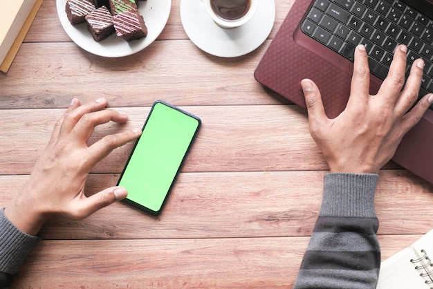 Top view of man hand using smart phone and typing on laptop