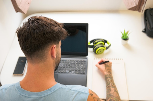 Top view of a man writing in a notebook and working wit a laptop at home