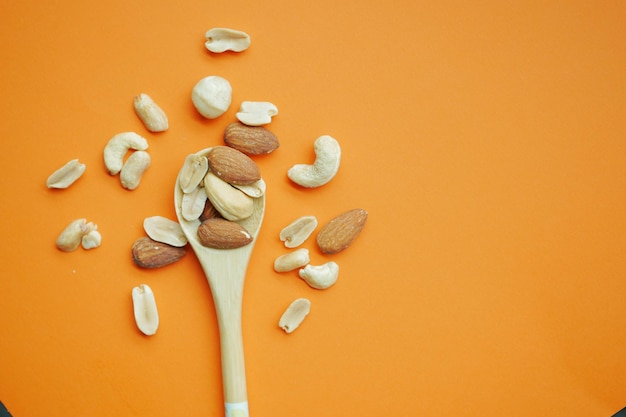 Top view of many mixed nuts on wooden spoon on orange background