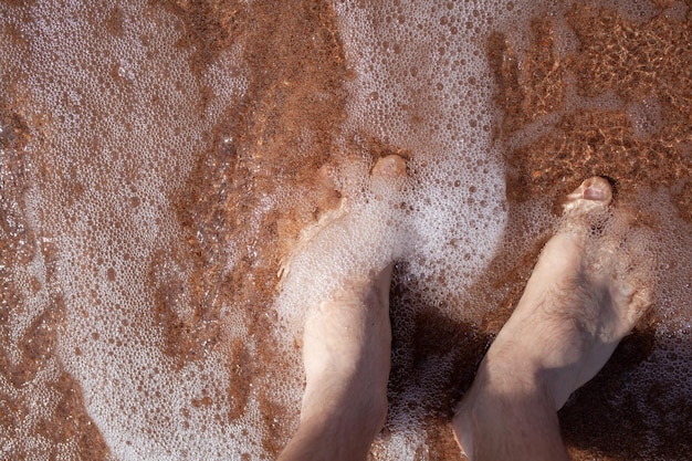 Top view of men39s legs in the sea A man is standing on the sand