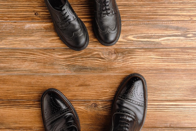 Top view of mens and childrens black classic shoes on wooden background fathers day concept