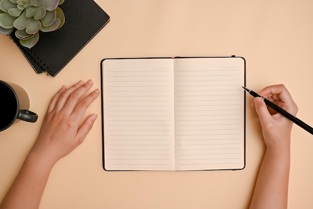 Top view Minimal beige workspace tabletop with female hand writing on her diary