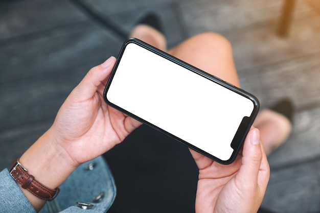 Top view mockup image of a woman holding a black mobile phone with blank white desktop screen