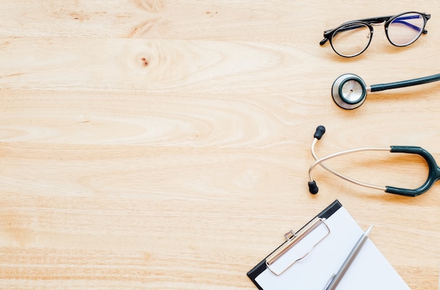 Top view of modern, sterile doctors office desk  with stethoscope on wooden background.