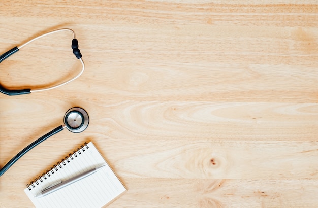 Top view of modern, sterile doctors office desk  with stethoscope on wooden background.