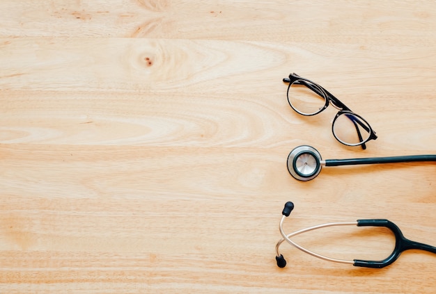 Top view of modern, sterile doctors office desk  with stethoscope on wooden background.