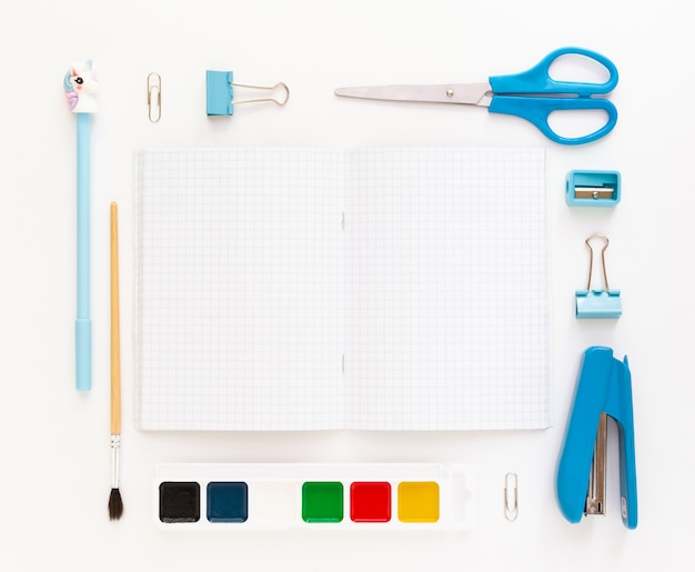 Top view of modern white blue office desktop with school supplies and stationery on table around empty space for text. Back to school concept flat lay with mockup