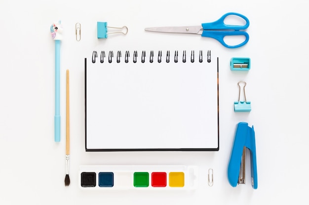 Top view of modern white blue office desktop with school supplies and stationery on table around empty space for text. Back to school concept flat lay with mockup