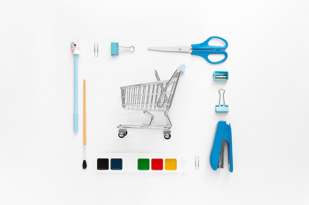 Top view of modern white blue office desktop with school supplies and stationery on table with basket or shopping trolley Back to school concept flat lay with mockup