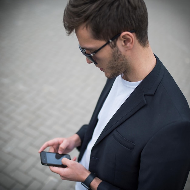 Top view of modern young man wearing black suit and sunglasses texting on the phone messages for his girlfirend in the street Technology and communication concept