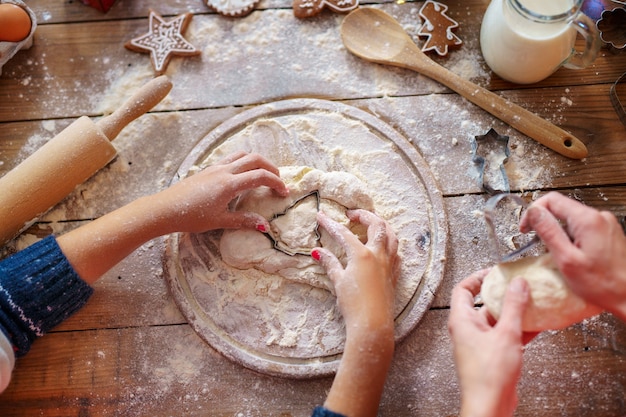 Top view of mother's and kid's hands making Christmas tree cookies. 