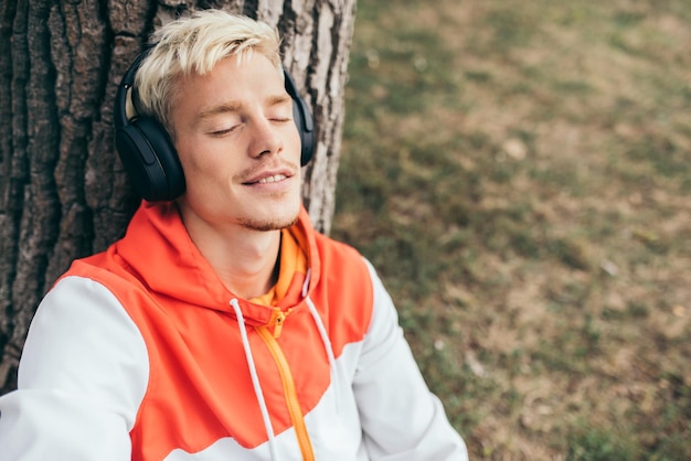 Top view of napping at nature young man in the park Blond guy in headphones listen to music sleeping on tree with copy space Leisure hobby relax and lifestyle concept