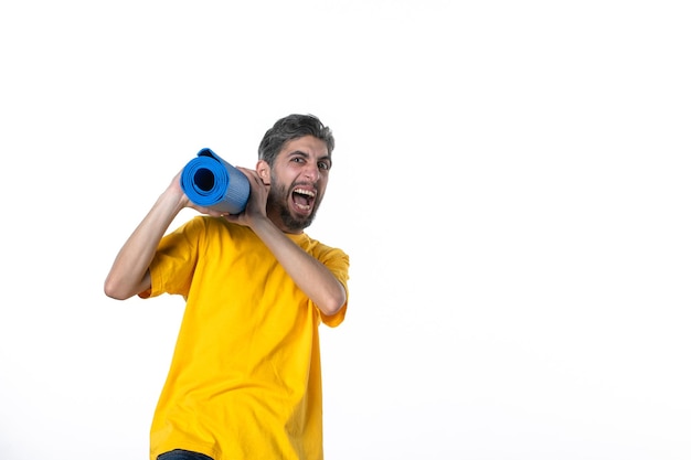 Top view of nervous young male in yellow shirt holding folded blue mat on white surface