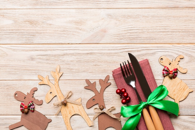 Top view of new year utensils on napkin with holiday decorations and reindeer on wooden background. Christmas dinner concept with copy space