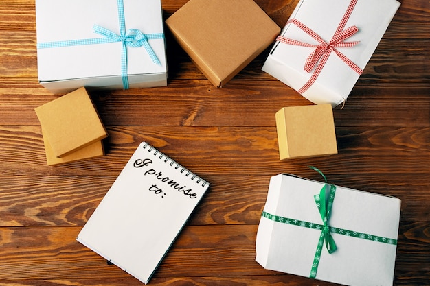 Top view of notebook and gift boxes with ribbons on wooden table piece of paper with inscription lis...