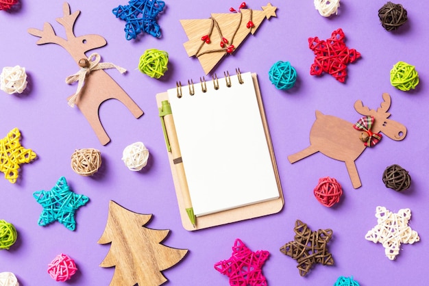 Top view of notebook New Year decorations on purple background Festive stars and balls Merry Christmas concept