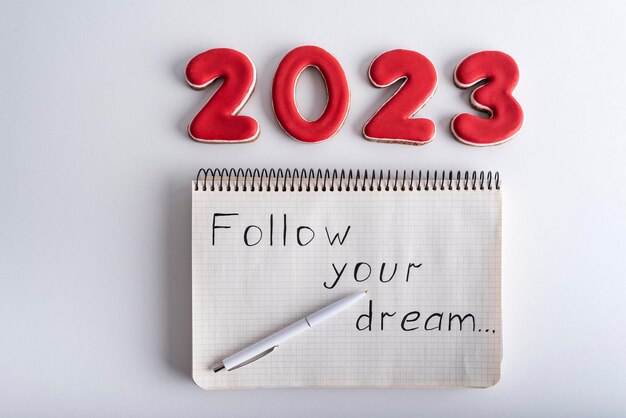 Top view numbers 2023 and notebook with words FOLLOW YOUR DREAM Wishlist for 2023