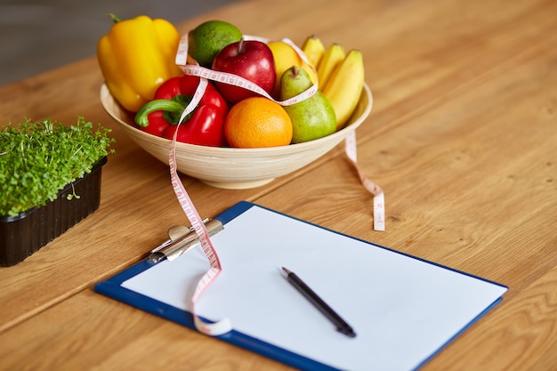 Top view of Nutritionist, dietitian workplace with measuring tape and bowl with healthy vegetables and fruits